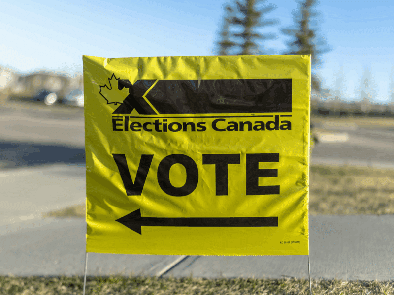 A vivid yellow sign from Elections Canada, displaying a maple leaf and bold black writing, signals a Canadian election voting site.